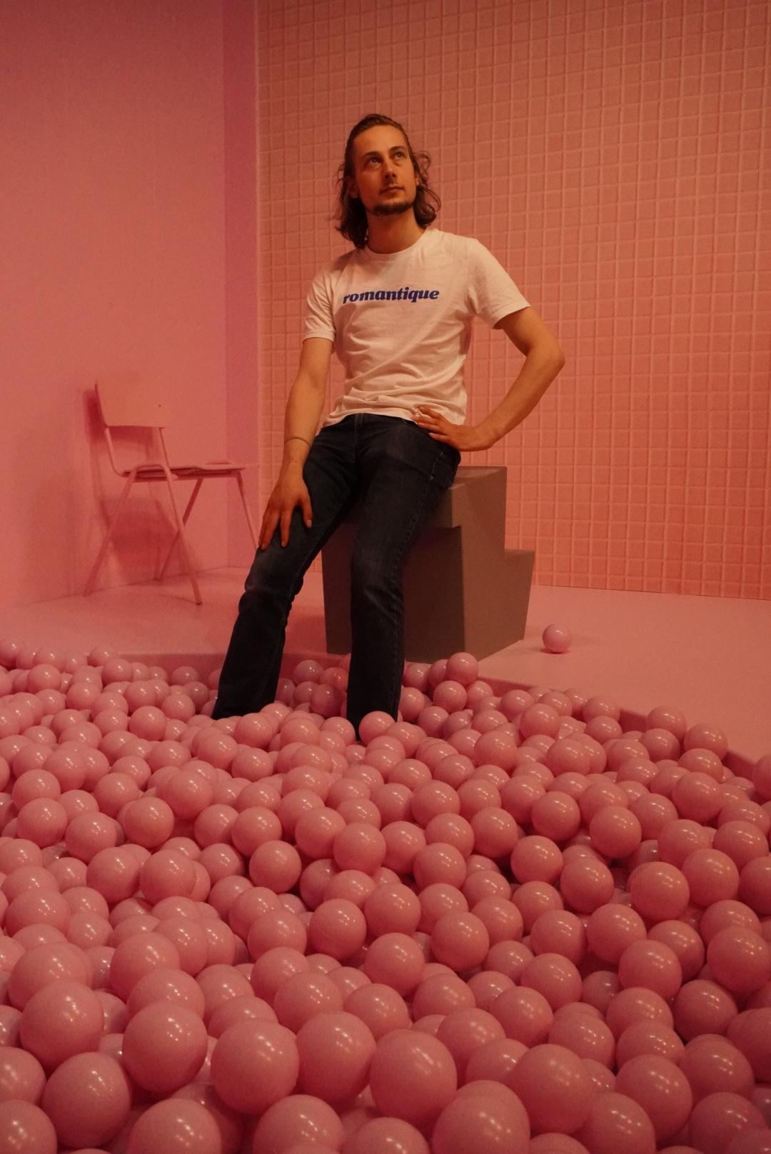 Auf dem Bild im Museum of Popcorn in Hamburg Hafencity sieht man einen jungen Mann in weißen T-Shirt und Jeans, der an die Decke blickt. Der Mann befindet sich in einem komplett rosafarbenen Raum. Im Vordergrund ist ein Bällebad, auf der linken Seite im Hintergrund steht ein Stuhl, links im Hintergrund eine blanke Wand, hinter ihm eine Kachelwand. Alles ist rosafarben. Nur der Springbock, auf dem der Mann sitzt, während seine Füße im Bällebad baumeln, ist in einem Grauton.